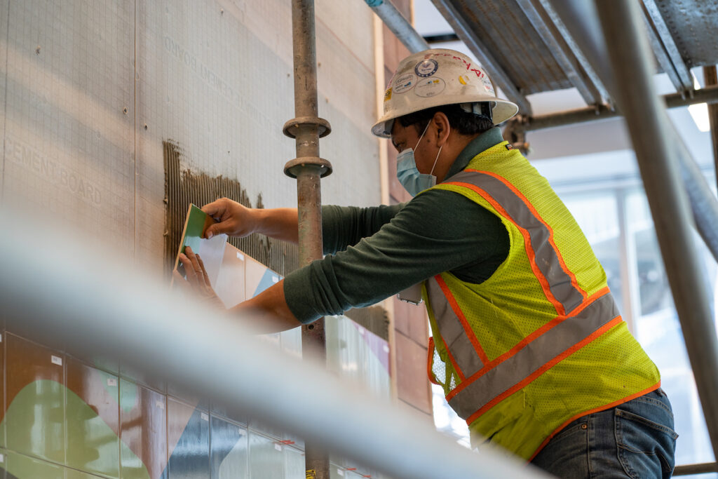 A person in construction gear attached ceramic tiles to a wall.
