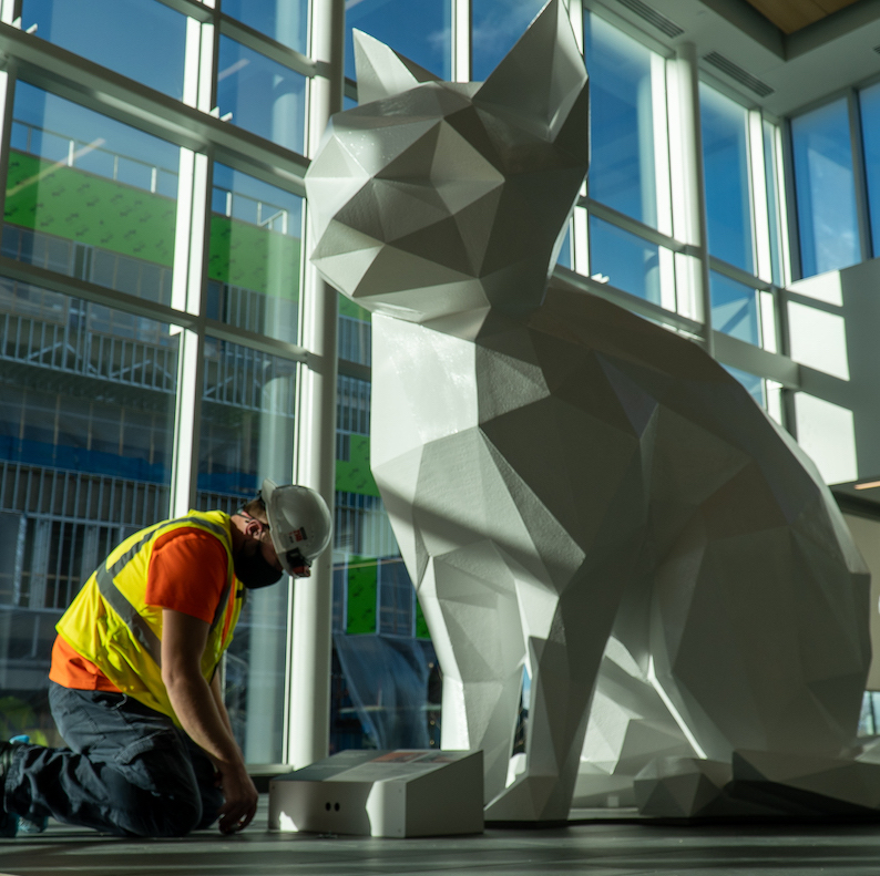 Construction worker kneels in front of a white cat statue.