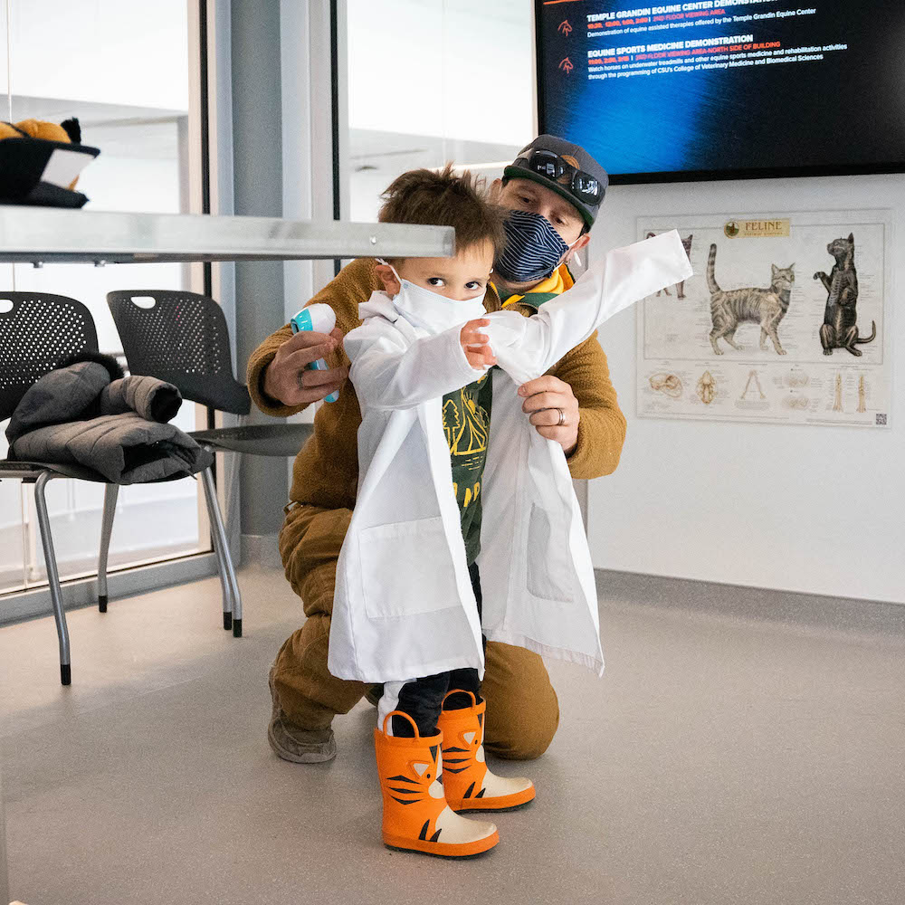 Child wears a lab coat and orange rain boots.