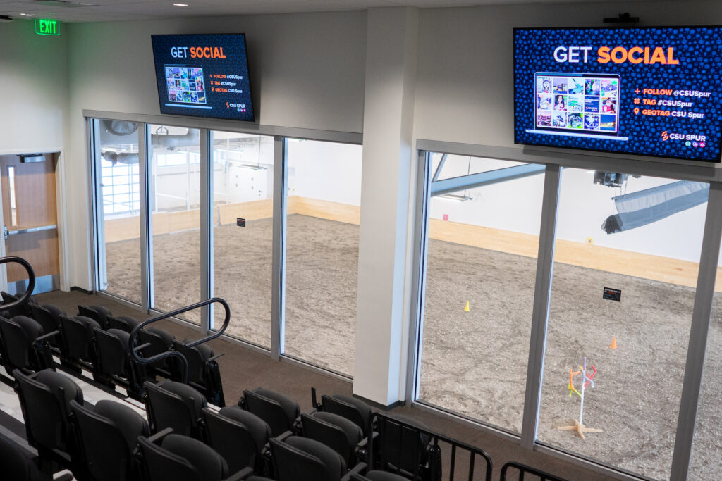 Room with two tvs and large windows looking down on an indoor arena.