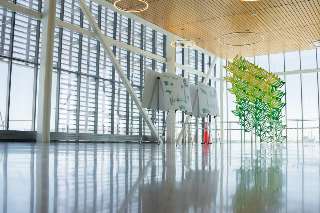 Indoor large space with floor to ceiling windows and a green and yellow art installation.