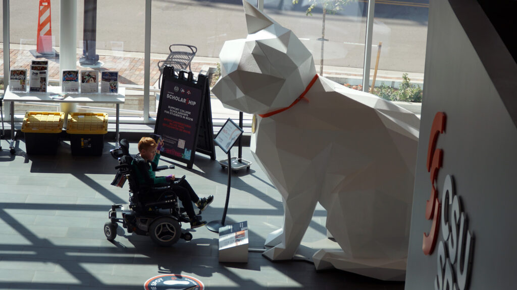 A child in a wheelchair approaches a large white cat statue.