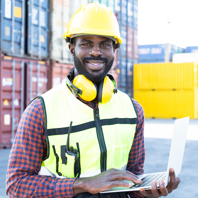 A man in a hard hat and reflective vest in front of a stack of shipping containers.