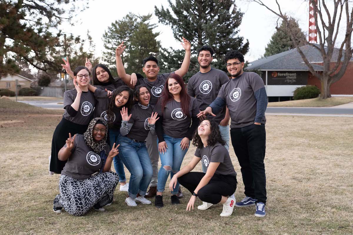 A group of young people in matching grey shirts pose for the camera outside.