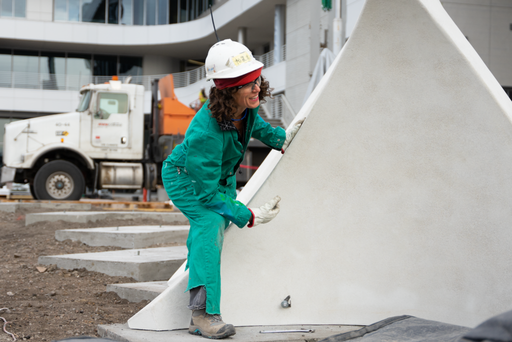 A person in a hard hat steps over the side of a piece of an art installation.