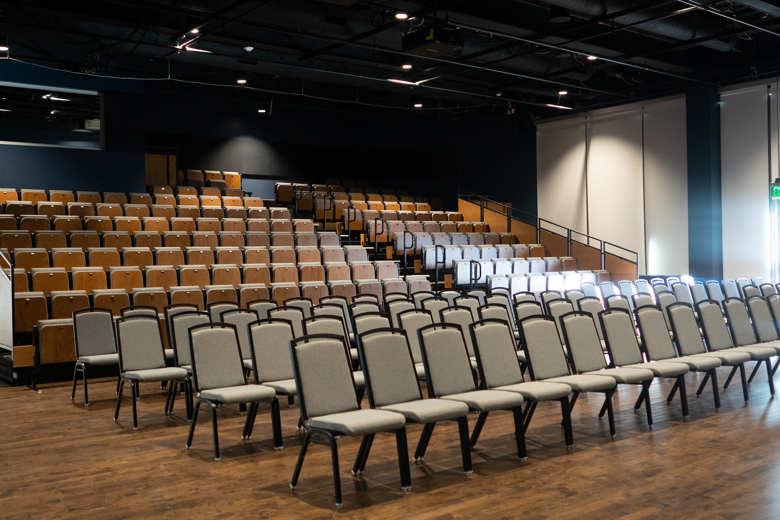 Theater space with bleacher seating and chairs up front.