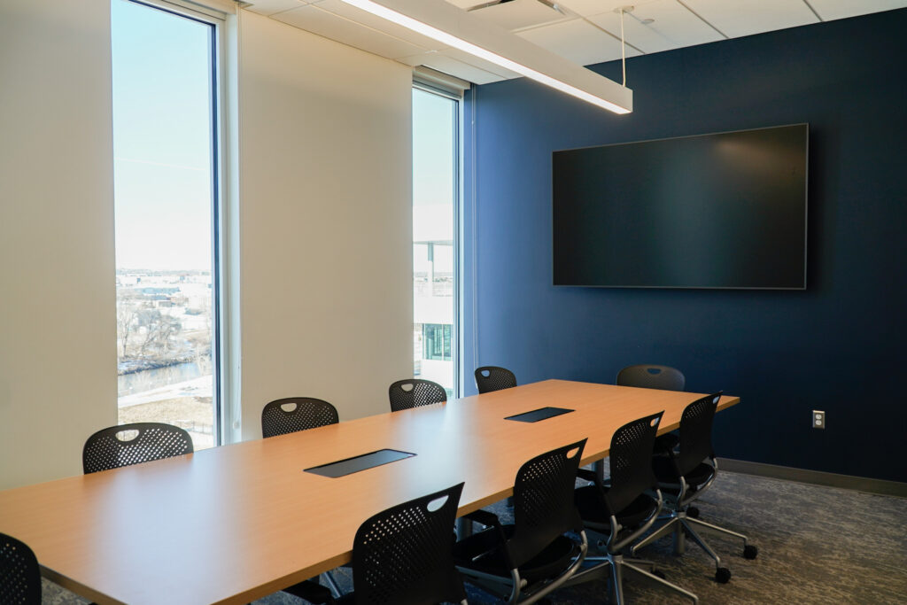 Conference room with a long table and wall-mounted screen.