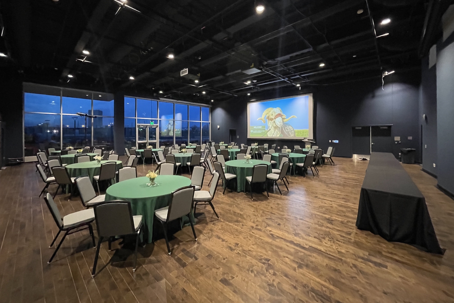 Theater space with wood flooring and large windows, set up with tables with green tablecloths.