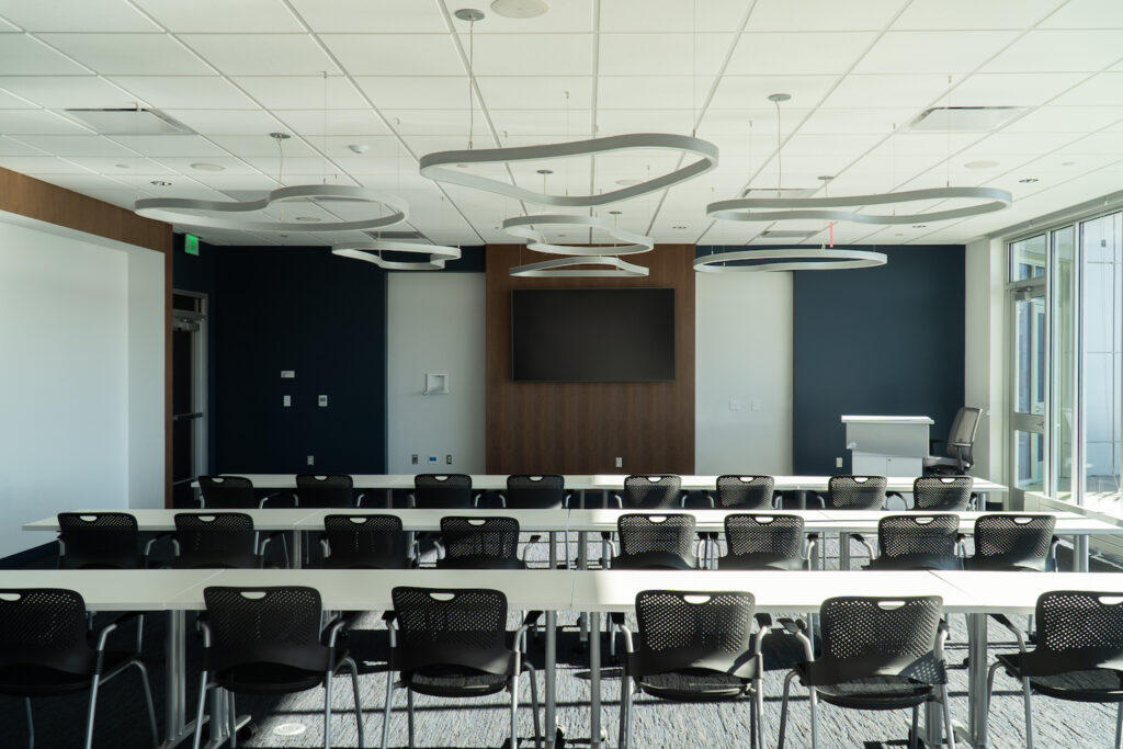 Conference room with rows of tables and chairs and a large screen.