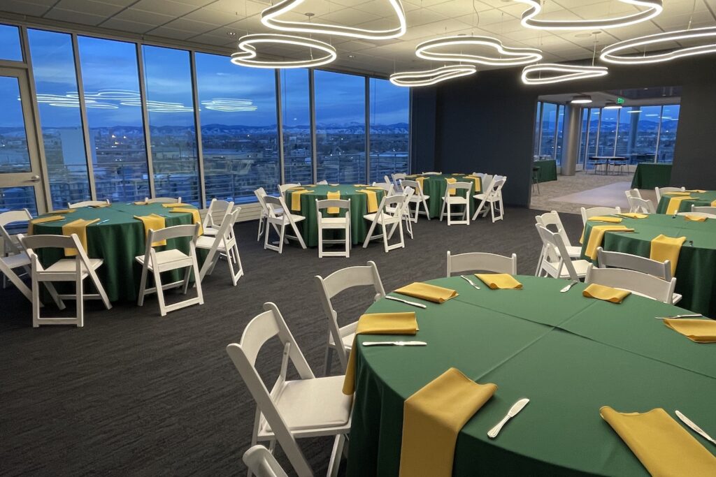 Room with large windows and several tables with green tablecloths.