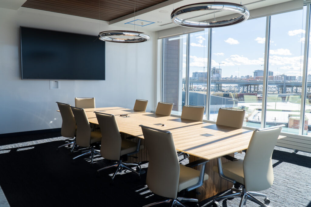 Conference room with a long table, a wall-mounted screen, and a view of downtown Denver.
