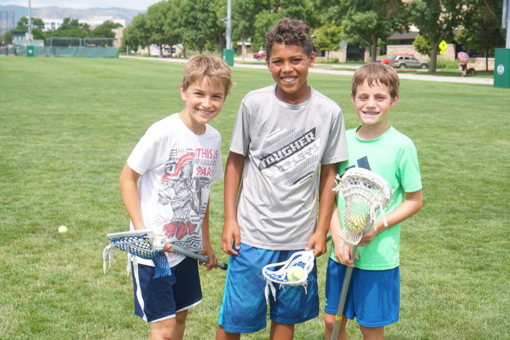 Three kids hold lacrosse sticks.