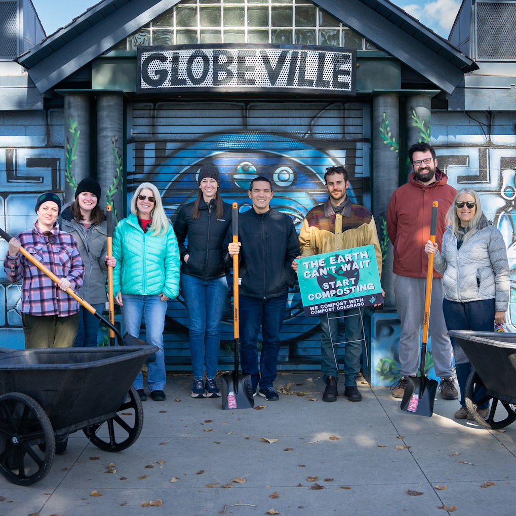 A group of people stand with wheelbarrows and shovels in front of a mural.