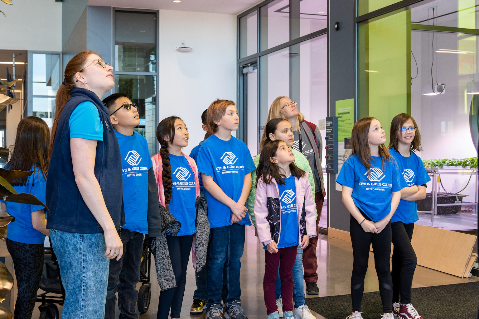 A group of students in blue t-shirts look up at the ceiling.