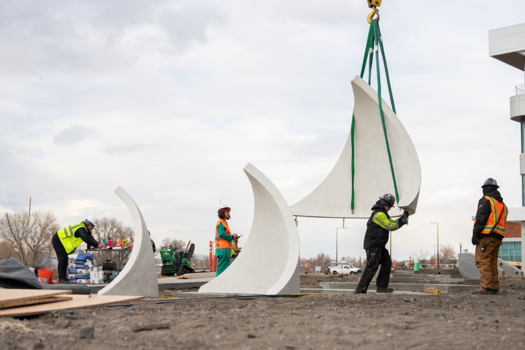 A large white concrete structure is lifted off the ground with rope.
