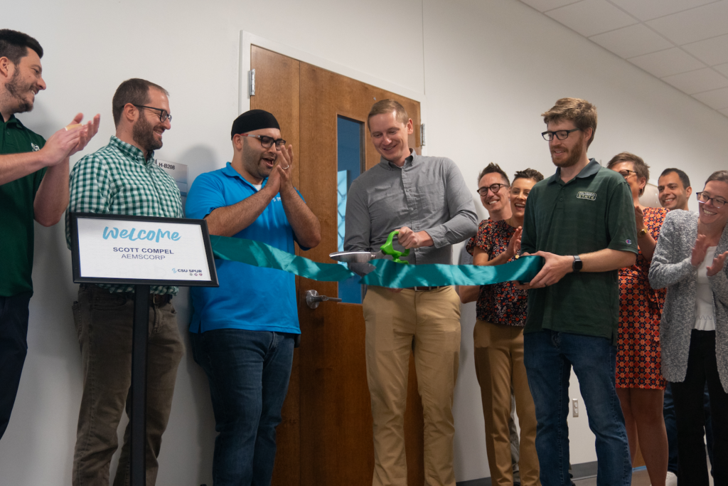 A group of people cut a blue and green ribbon.