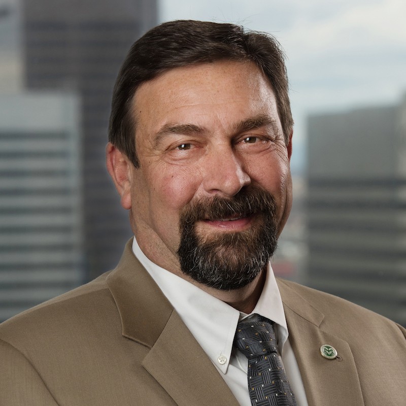 Man with dark hair and a goatee and a CSU Rams pin on a tan blazer.