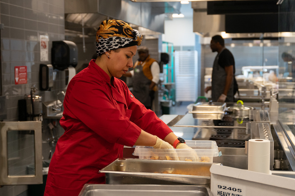 A person with a red shirt and a head wrap working in a kitchen.