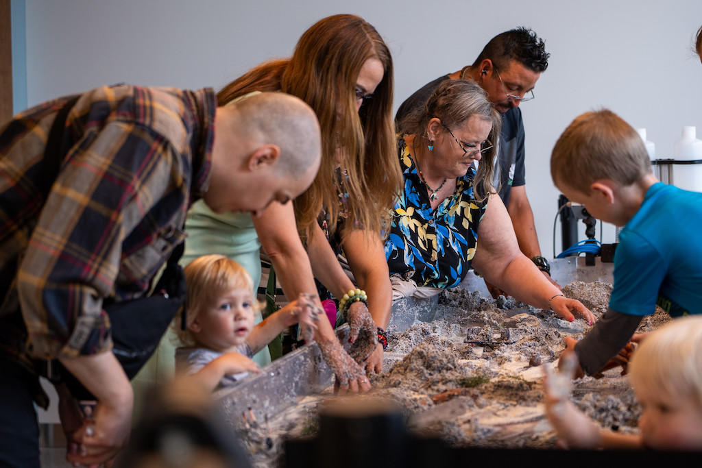 People interact with a stream table full of sand.