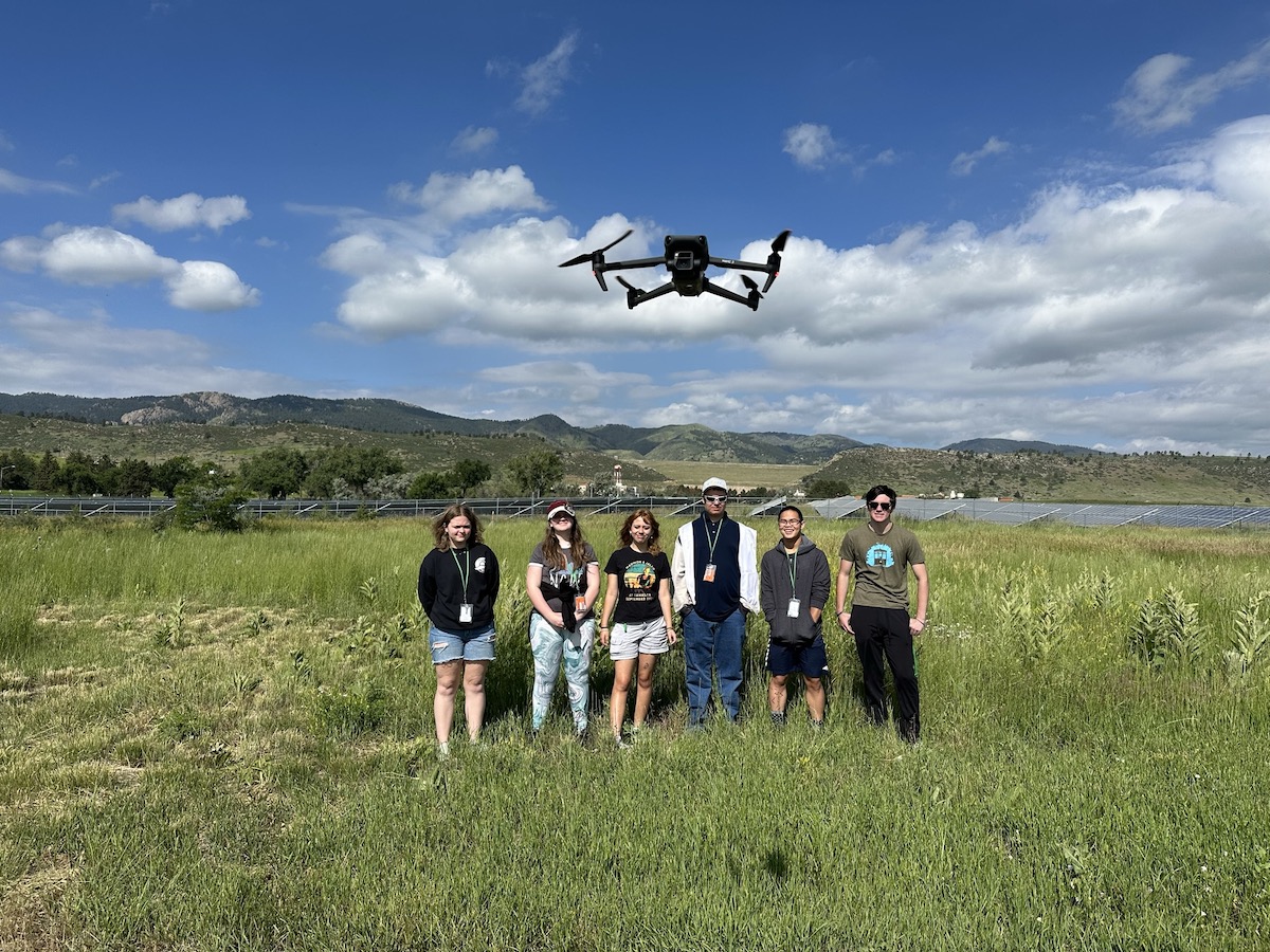 Group standing in a field under a black drone.