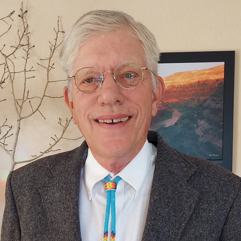Man in a white shirt, grey jacket, and turquoise bolo tie.