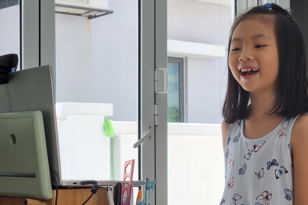A girl smiles at a computer.