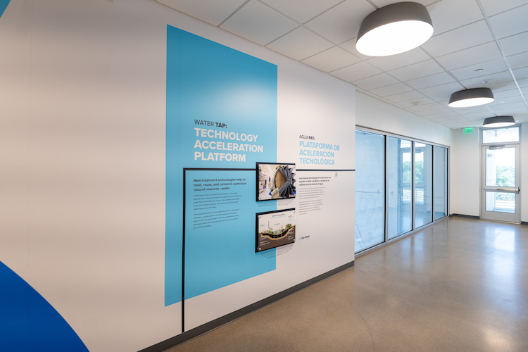 Wall-mounted panels showing information about the Water TAP with windows to look into the lab.