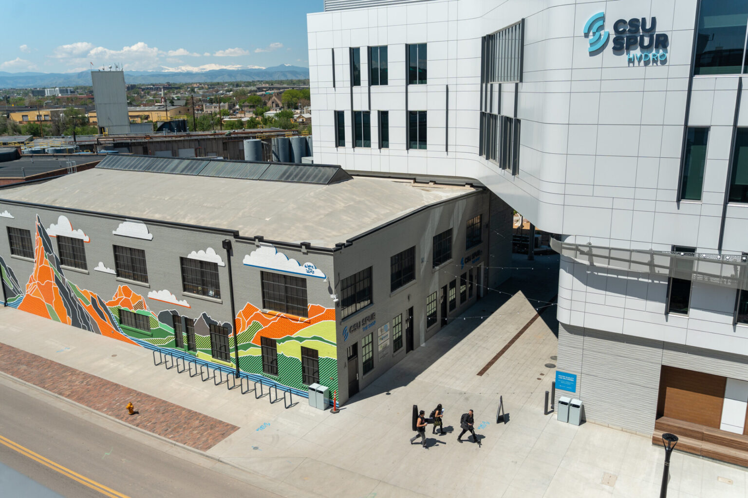 Aerial view of people walking in front of the Hydro building and a colorful mural on the side of the Shop.