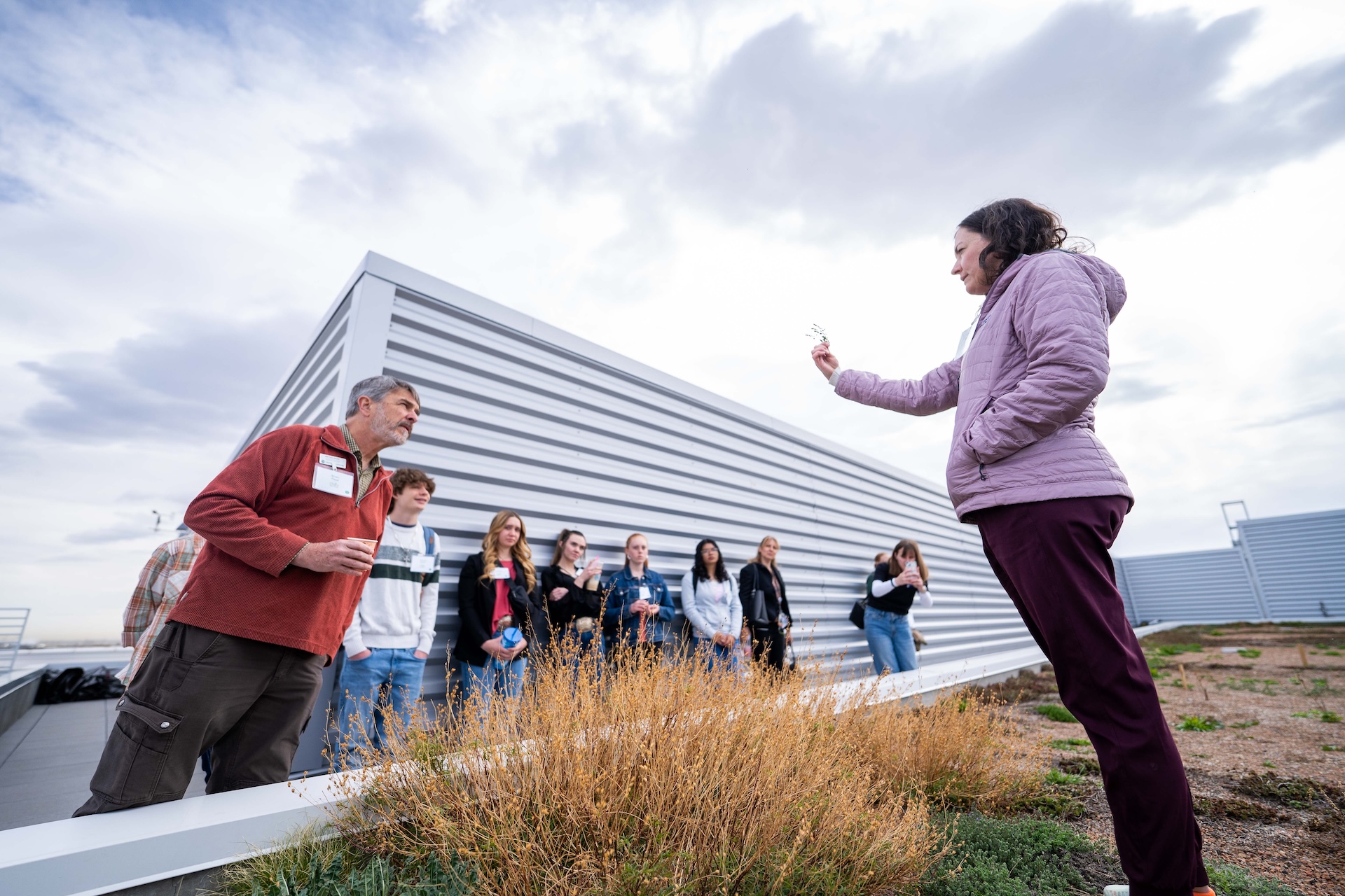 A woman talks to a group of adults in a rooftop garden.