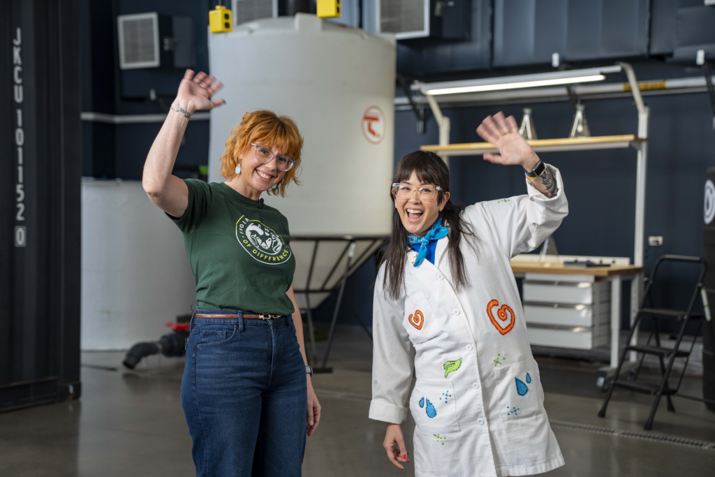 Two people, one in a CSU shirt and one in a lab coat, wave to the camera.